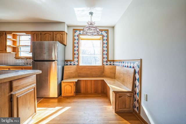 kitchen with sink, light hardwood / wood-style flooring, stainless steel fridge, pendant lighting, and backsplash