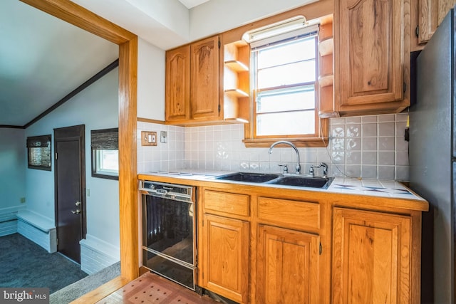 kitchen featuring vaulted ceiling, tile countertops, stainless steel refrigerator, dishwasher, and sink