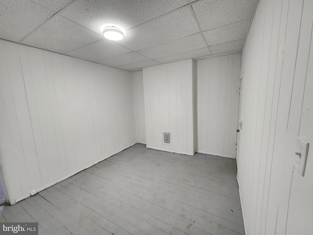 empty room featuring a paneled ceiling, light hardwood / wood-style flooring, and wood walls