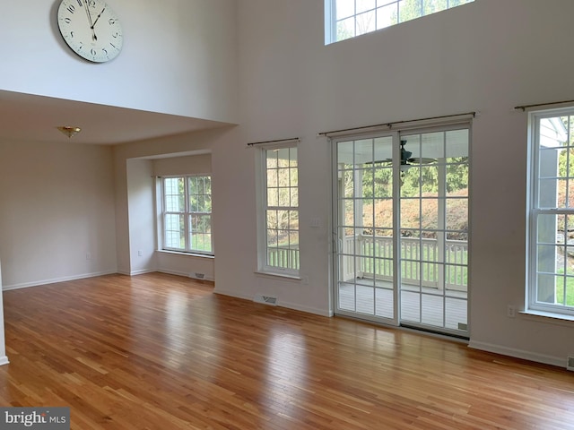 unfurnished living room with a high ceiling, light wood-type flooring, and ceiling fan