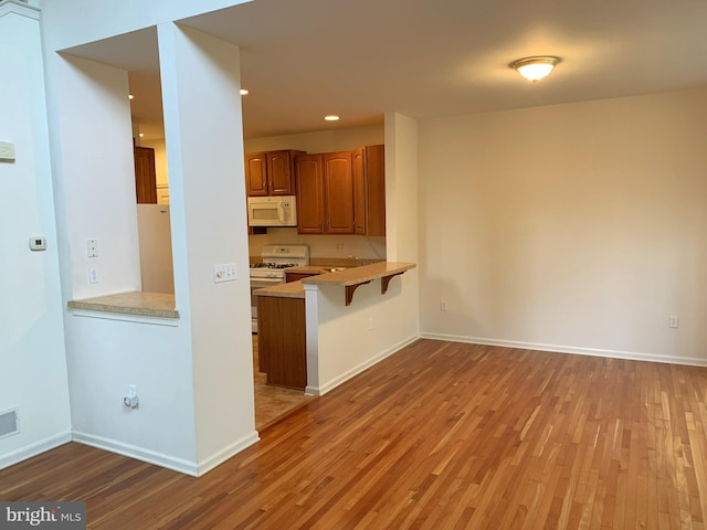 kitchen with kitchen peninsula, a kitchen breakfast bar, white appliances, and light hardwood / wood-style flooring