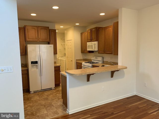 kitchen featuring a kitchen bar, kitchen peninsula, white appliances, washing machine and clothes dryer, and light hardwood / wood-style floors