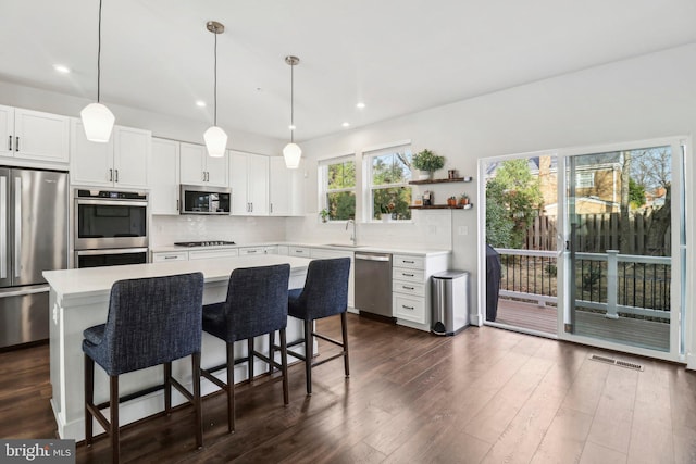 kitchen featuring stainless steel appliances, white cabinets, dark hardwood / wood-style floors, a kitchen island, and hanging light fixtures