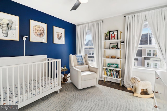 bedroom with hardwood / wood-style flooring, ceiling fan, multiple windows, and a nursery area