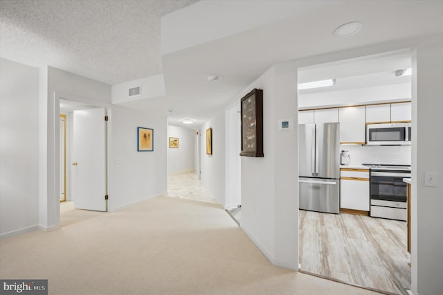 hallway featuring light carpet and a textured ceiling