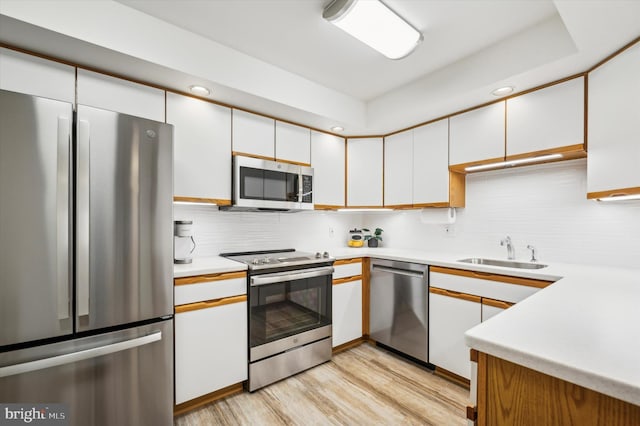 kitchen with light wood-type flooring, tasteful backsplash, stainless steel appliances, sink, and white cabinetry