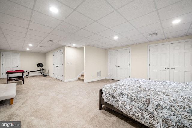 bedroom featuring light colored carpet, a drop ceiling, and multiple closets