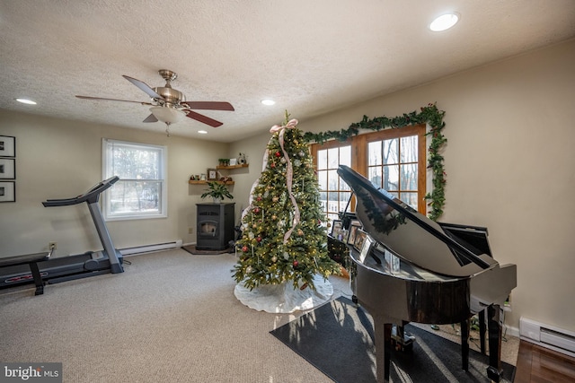 exercise room featuring a wood stove, ceiling fan, a baseboard radiator, and a textured ceiling