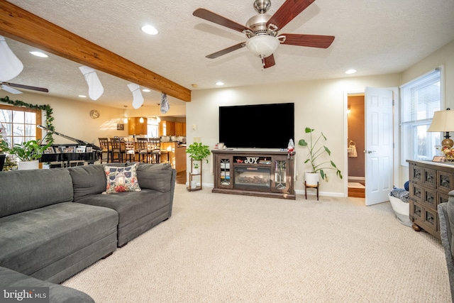 living room with beamed ceiling, ceiling fan, a textured ceiling, and carpet