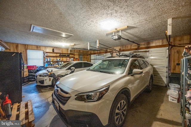 garage with black refrigerator, a garage door opener, and wood walls