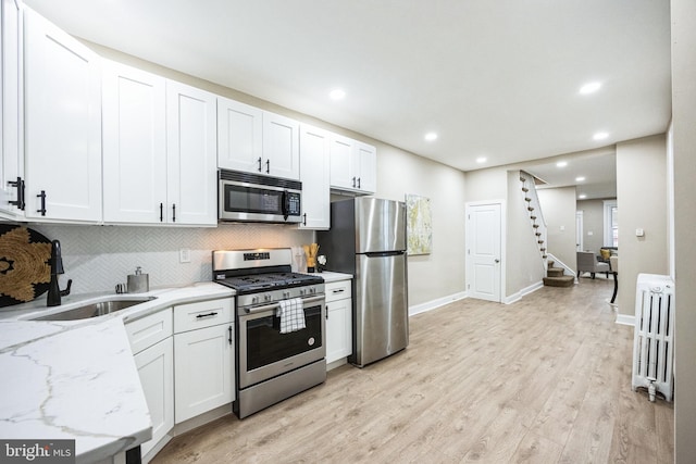 kitchen with radiator heating unit, white cabinets, stainless steel appliances, and sink