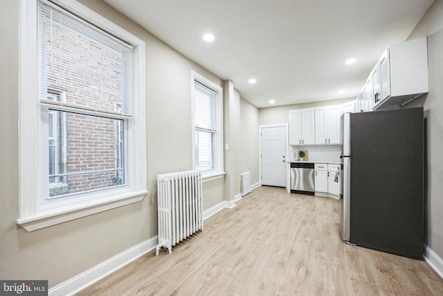 kitchen featuring radiator heating unit, stainless steel appliances, white cabinetry, and light hardwood / wood-style flooring