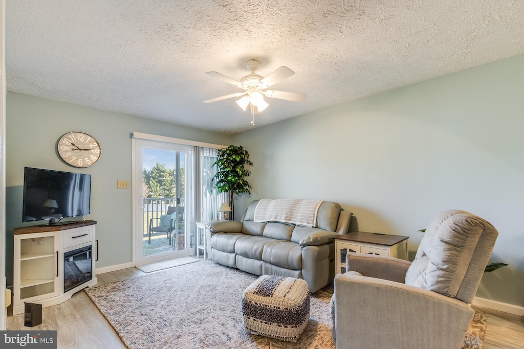 living room with ceiling fan, a textured ceiling, and light hardwood / wood-style flooring