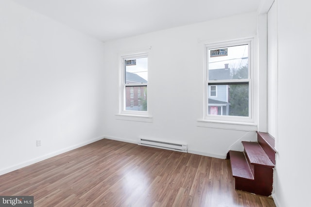 empty room with hardwood / wood-style floors, baseboard heating, and a wealth of natural light