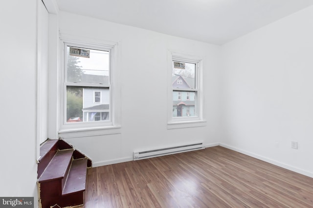 unfurnished room featuring hardwood / wood-style flooring and a baseboard heating unit