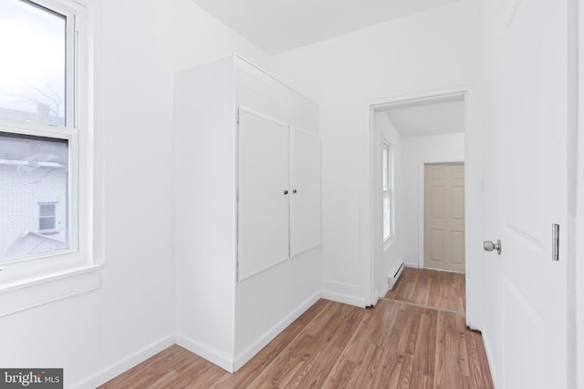 hall with baseboard heating, a wealth of natural light, and light wood-type flooring