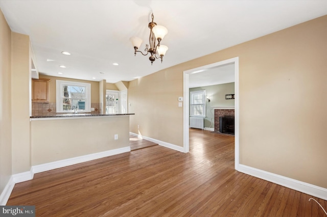 unfurnished living room with radiator, a fireplace, sink, a chandelier, and hardwood / wood-style flooring