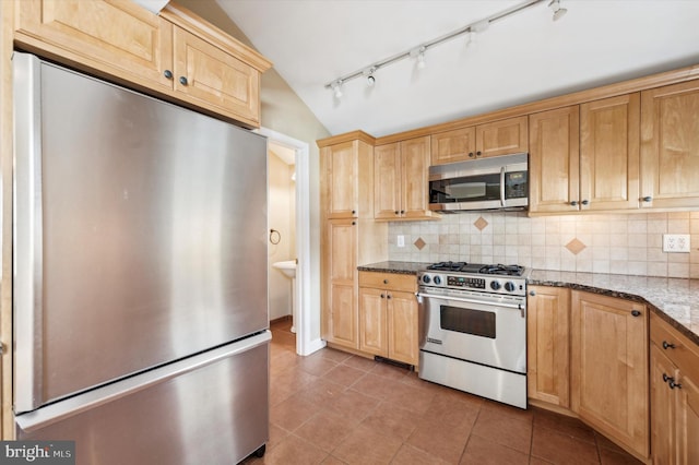 kitchen featuring tasteful backsplash, appliances with stainless steel finishes, vaulted ceiling, and dark stone countertops