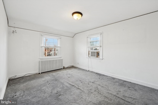 carpeted empty room with cooling unit, radiator heating unit, and a wealth of natural light