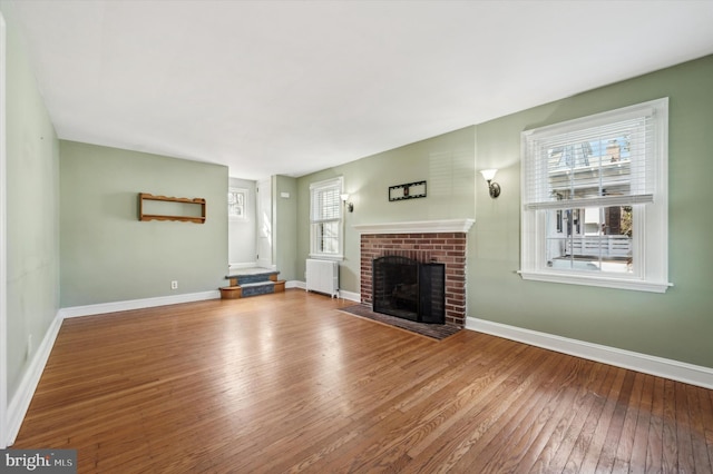 unfurnished living room with radiator heating unit, wood-type flooring, and a brick fireplace