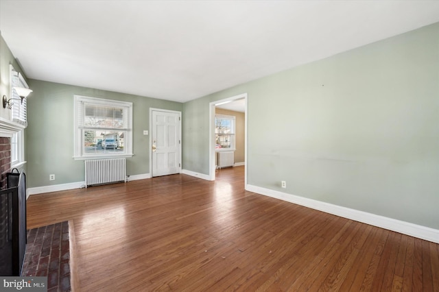 unfurnished living room featuring dark wood-type flooring, radiator heating unit, and a brick fireplace