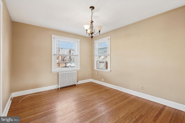 spare room with radiator, hardwood / wood-style floors, an inviting chandelier, and cooling unit