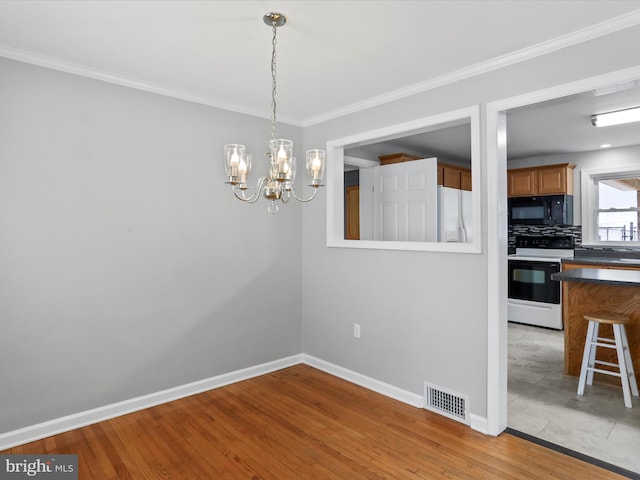 unfurnished dining area featuring light wood-type flooring, ornamental molding, and a chandelier