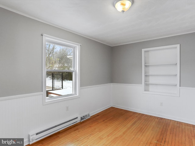 empty room with hardwood / wood-style floors, built in features, and a baseboard radiator