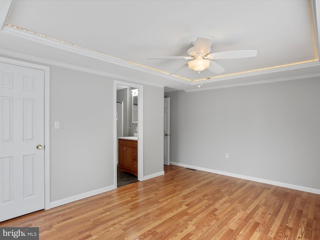 unfurnished bedroom featuring ceiling fan, ornamental molding, light hardwood / wood-style flooring, and a tray ceiling