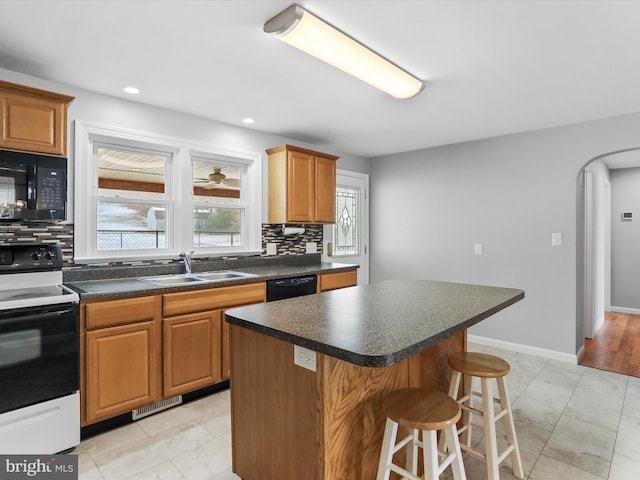 kitchen featuring sink, tasteful backsplash, a kitchen bar, a kitchen island, and black appliances