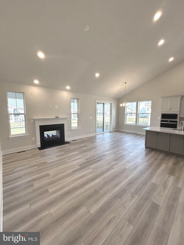 unfurnished living room with plenty of natural light, light hardwood / wood-style flooring, sink, and vaulted ceiling