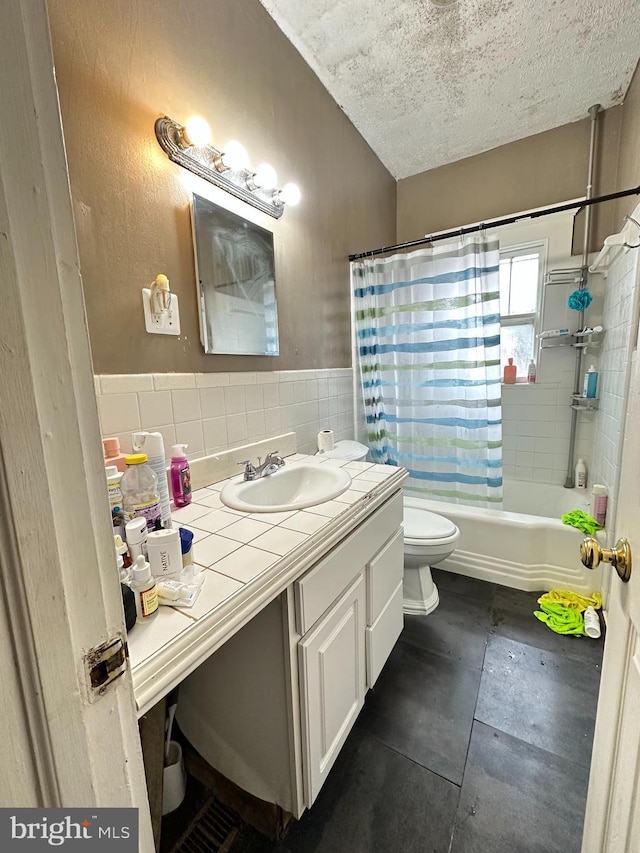 full bathroom with shower / bath combo, vanity, toilet, a textured ceiling, and tile walls