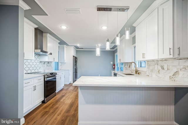 kitchen with kitchen peninsula, wall chimney exhaust hood, hanging light fixtures, and appliances with stainless steel finishes