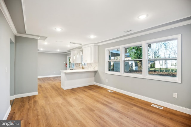 interior space with kitchen peninsula, decorative backsplash, ornamental molding, light hardwood / wood-style flooring, and white cabinetry