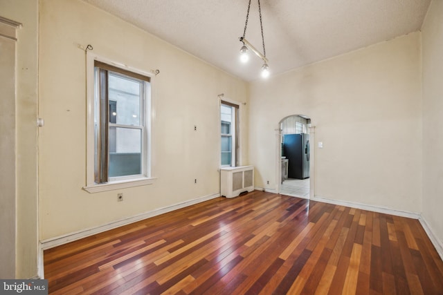 spare room featuring dark hardwood / wood-style floors, radiator heating unit, and a textured ceiling