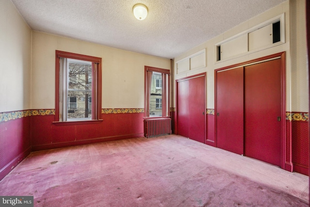 unfurnished bedroom featuring multiple closets, light carpet, radiator heating unit, and a textured ceiling