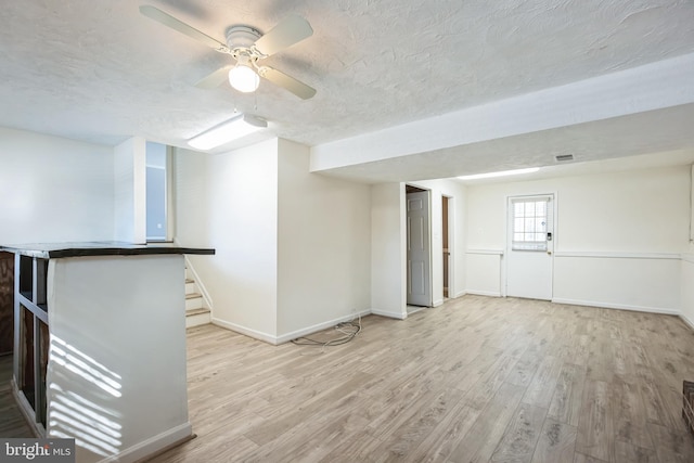 basement featuring ceiling fan, light hardwood / wood-style floors, and a textured ceiling