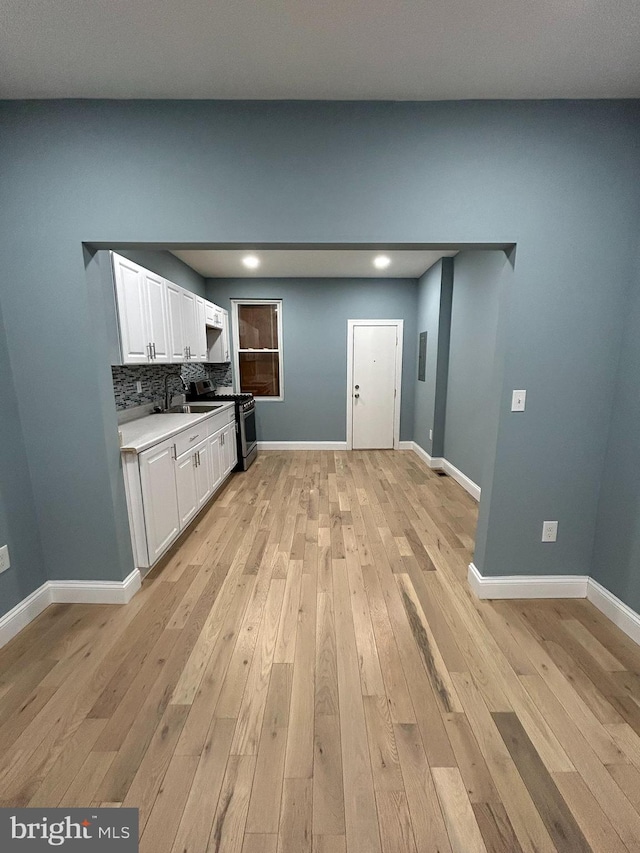 kitchen with light hardwood / wood-style floors, stainless steel gas range oven, white cabinetry, and backsplash