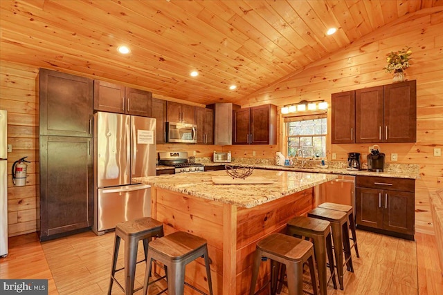 kitchen featuring a center island, a kitchen breakfast bar, vaulted ceiling, appliances with stainless steel finishes, and light wood-type flooring