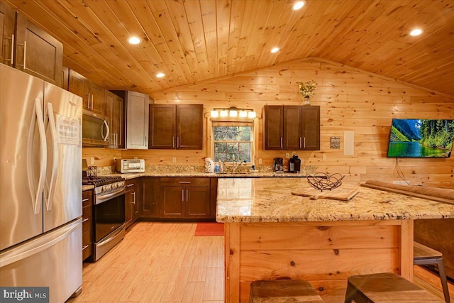 kitchen featuring wood walls, light stone countertops, stainless steel appliances, and vaulted ceiling