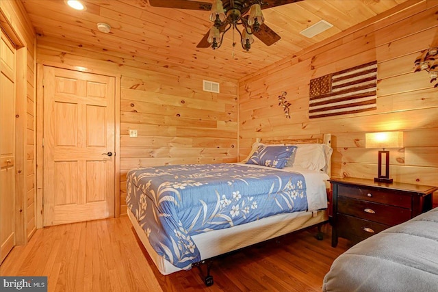 bedroom with ceiling fan, wooden walls, and light hardwood / wood-style flooring