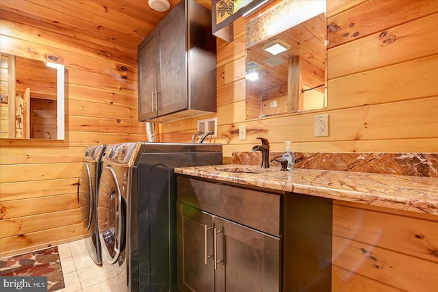 laundry area featuring washing machine and clothes dryer, wood walls, light tile patterned floors, and cabinets