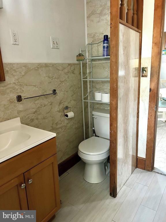 bathroom featuring tile patterned flooring, vanity, toilet, and tile walls