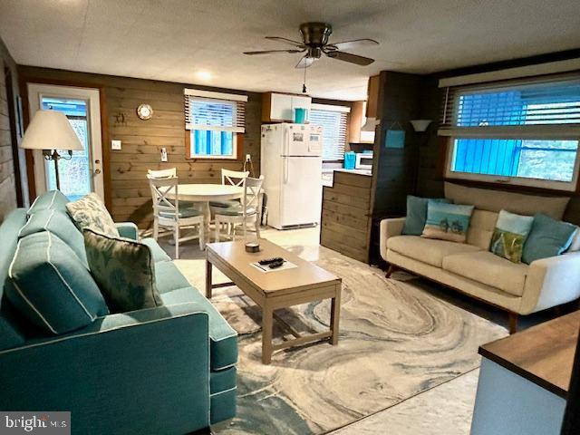 living room with wooden walls, ceiling fan, and a textured ceiling