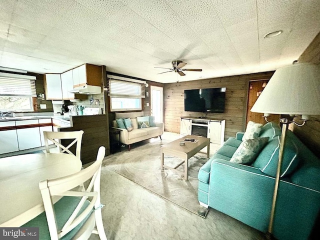 living room with wooden walls, ceiling fan, and a healthy amount of sunlight