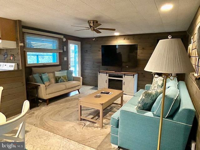 living room featuring ceiling fan, wood walls, and a textured ceiling