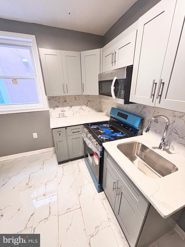 kitchen with light stone countertops, tasteful backsplash, gray cabinetry, stainless steel appliances, and sink