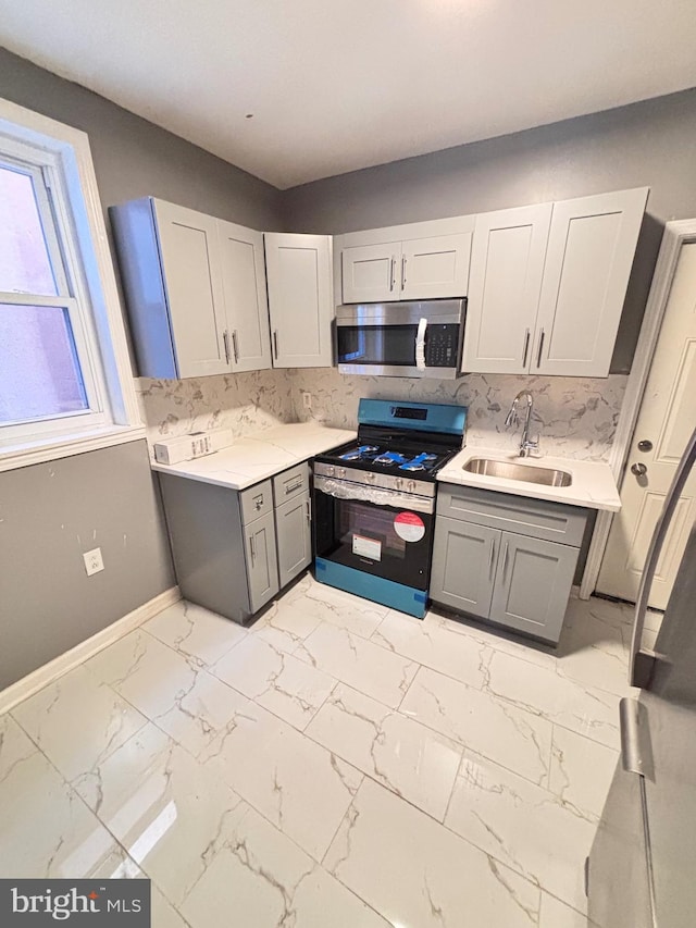 kitchen featuring backsplash, gray cabinetry, sink, and stainless steel appliances