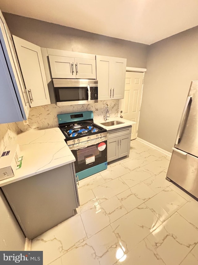 kitchen featuring light stone countertops, appliances with stainless steel finishes, backsplash, sink, and white cabinets