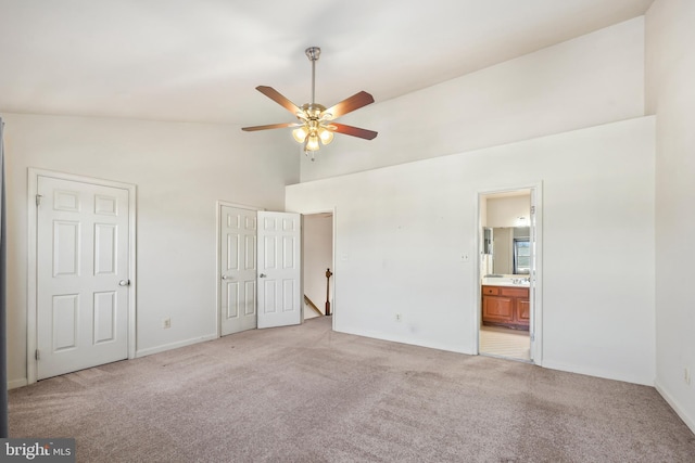 unfurnished bedroom featuring light carpet, ensuite bath, high vaulted ceiling, and two closets